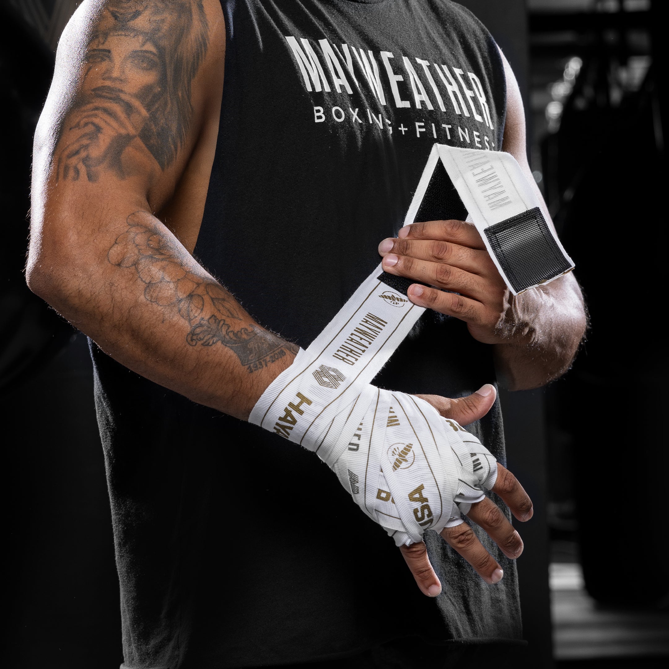 Vista frontale della mano di un fighter con la fasciatura completa eseguita utilizzando la benda elasticizzata bianca e oro Mayweather Hayabusa 180 pollici, con il logo 'MAYWEATHER' visibile sull'area del polso