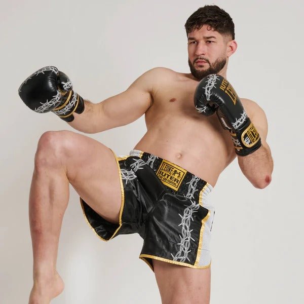 Atlet în ipostaza loviturii de Muay Thai care arată flexibilitatea pantalonilor scurți Barbed Wire