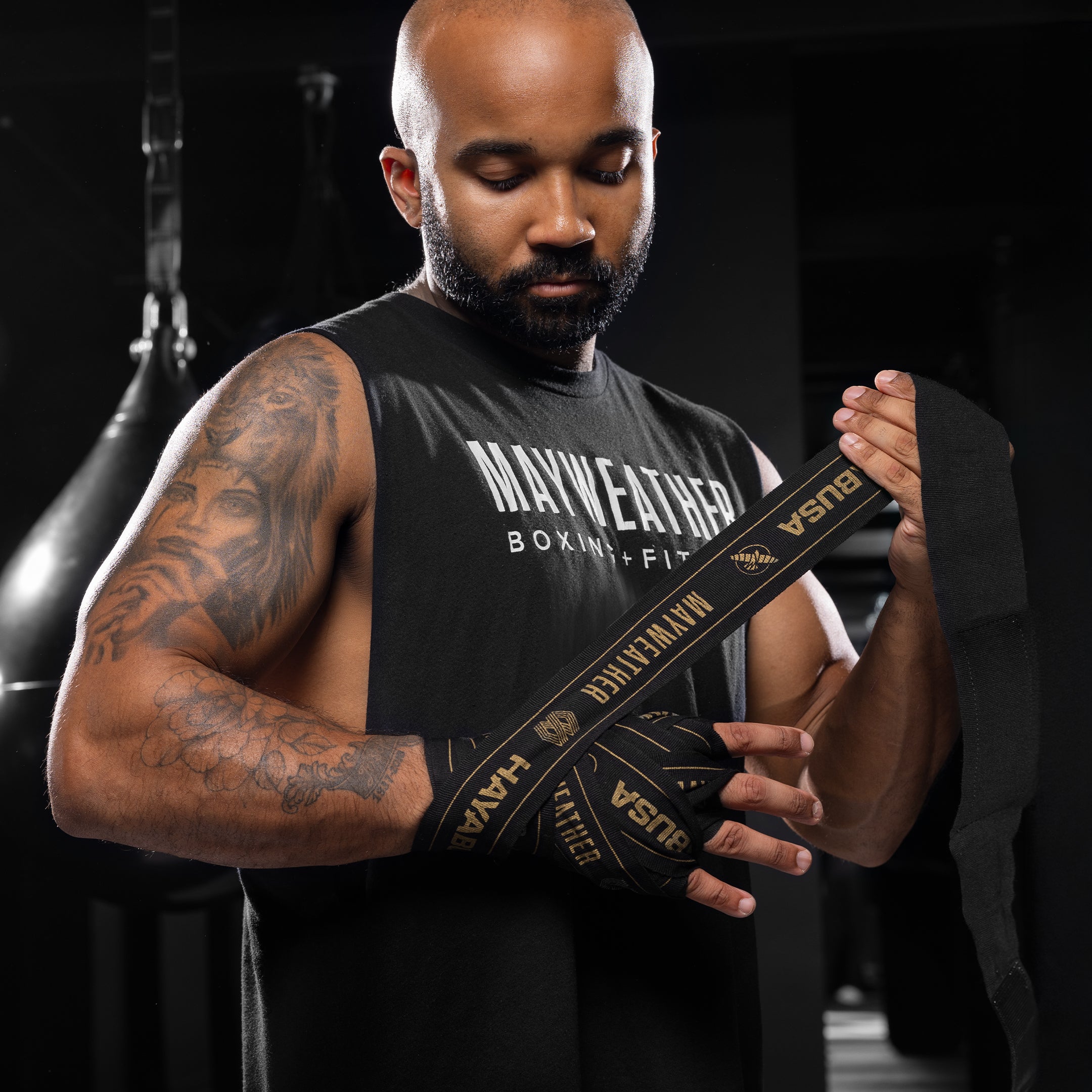 Primo piano di una mano di un boxer interamente fasciata con la benda elasticizzata Mayweather Hayabusa 180 pollici nera e oro, che mette in risalto il passante per il pollice, l'allineamento delle nocche e la chiusura a strappo con logo