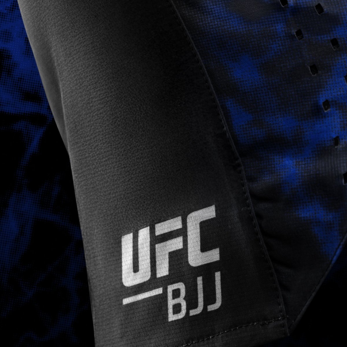Detalle lateral del logo oficial de UFC BJJ impreso en el pantalón corto negro y azul para mujer.
