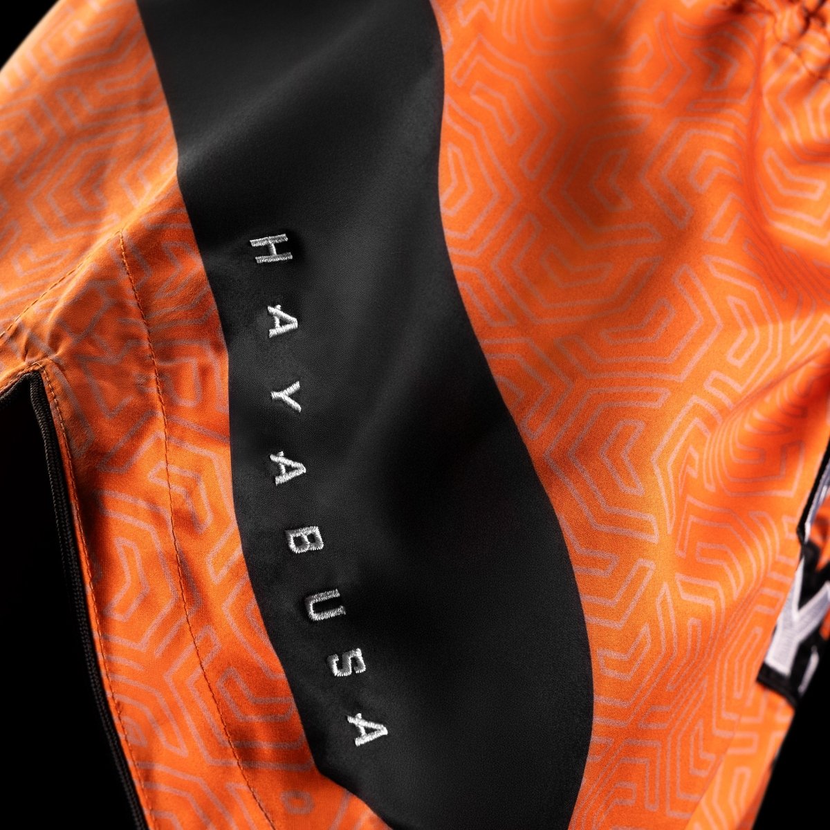 Detalj av den glänsande finishen och tygmotståndet hos de orangea Hayabusa Core-shortsen