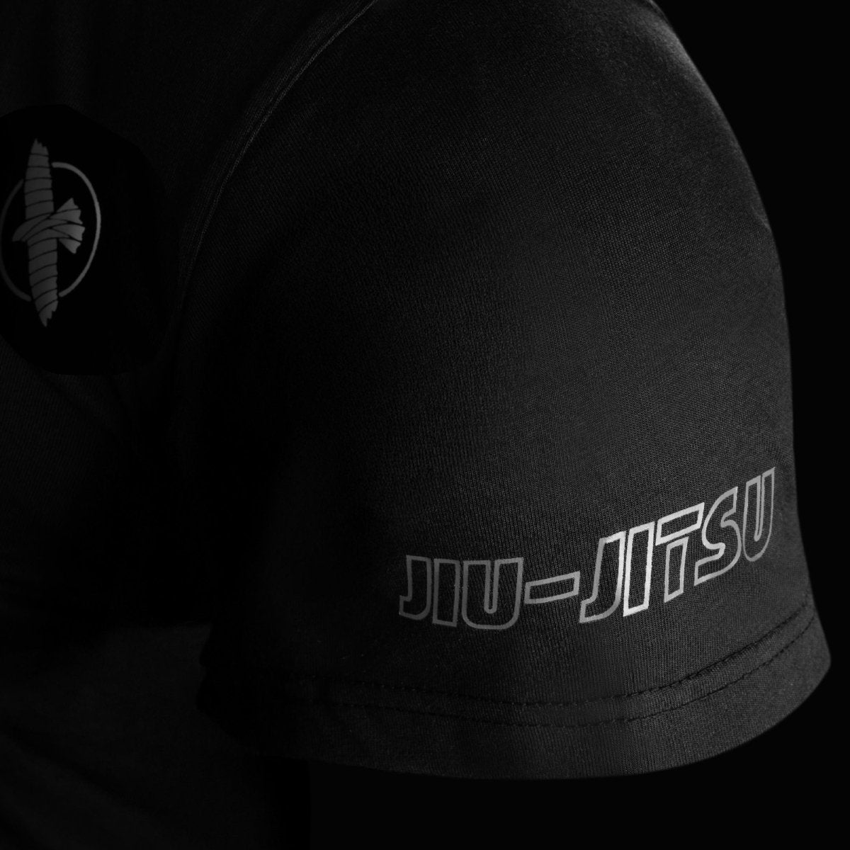 Detaliu în prim plan al mânecii tricoului negru Hayabusa UFC BJJ, care arată cusăturile întărite și logo-ul șoimului brodat